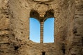 Inside of ancient stone brick ruin building with arched window and blue sky.