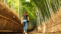 Inside the Arashiyama Bamboo Grove park of Japan, a paved path, with sides of straw and wood, guides this visitor into the forest.