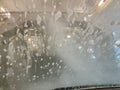 Inside automatic conveyorized tunnel car wash. View from inside car, windshield with water drops and soap foam. Royalty Free Stock Photo