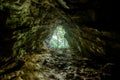 Inside a dark wet cave with the illuminated exit in sight