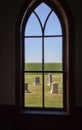 Inside looking out of arched church window looking at grave yard.