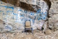 Inside the natural carved cave there is an old chair and a turtle on the ground. Street graffiti of unknown origin.