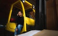 Inside a warehouse, a young woman businessman sits on the step of a yellow forklift and speaks on the phone. Logistics Royalty Free Stock Photo