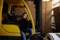 Inside the warehouse, a young woman businessman sits on the step of a yellow forklift and speaks on the phone. The sun is shining Royalty Free Stock Photo
