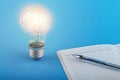 Insight concept. coming of ideas at work. glowing light bulb and diary with a pen on a blue background.