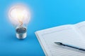 Insight concept. coming of ideas at work. glowing light bulb and diary with a pen on a blue background.