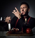 Insolent man in black shirt and suspenders at table with fresh pomegranate and juice, holds knife and licks his finger Royalty Free Stock Photo