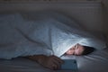 Portrait of sleepy tired man lying in bed under the blanket using smartphone at late night, can not sleep. Royalty Free Stock Photo