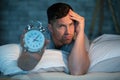 insomniac man in bed showing alarm clock