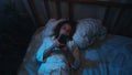 Insomniac young woman lying in bed scrolling smartphone at night.