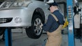 Inspection of the chassis of the car. A young mechanic in uniform works in a car service with a lifted car. Car repair Royalty Free Stock Photo