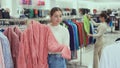 Girl stopped near leisure wear showcase, holds eiderdown bathrobe hanger in hands, examines product