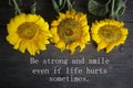 Inspirational motivational quote - Be strong and smile even if life hurts sometimes. With yellow sun flowers decoration on rustic