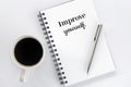 Inspirational motivational words - Improve yourself, on a spiral notepaper book with silver pen and a cup of black morning coffee.
