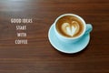 Inspirational positive quote `Good ideas start with coffee` with heart shape latte coffee and wooden desk background.