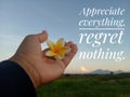 Inspirational quote - Appreciate everything, regret nothing. With hand holding a flower on blue morning sky over the mountain.