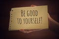 Inspirational quote - Be good to yourself. With a paper note in young woman hand on light brown background. Reminder, note to self Royalty Free Stock Photo