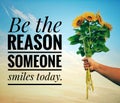Inspirational quote - Be the reason someone smiles today. With a hand holding a bunch of sunflowers against bright blue sky.
