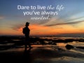 Inspirational quote - Dare to live the life you`ve always wanted. With silhouette of a adventurous woman standing alone on beach.