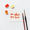 Inspirational quote do what you love , watercolor cuvettes, paint brushes on a white background. Artist workspace.
