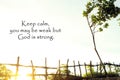 Inspirational quote- Keep calm, you may be weak but God is strong. With natural wooden fence on cliff edge with sun shine between