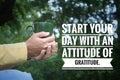 Inspirational quote - Start your day with an attitude of gratitude. With person holding a cup of tea or coffee in hands on green