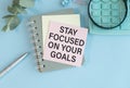 Inspirational quote - Stay focused on your goals. With a text message on a pink sticker on a green notepad with a pen, a Royalty Free Stock Photo