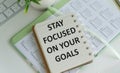 Inspirational quote - Stay focused on your goals. With text message on white paper book, pen, a cup of morning coffee, flower. Royalty Free Stock Photo