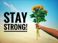 Inspirational quote - Stay strong.  With hand holding bouquet of sunflowers against bright blue sky background. Royalty Free Stock Photo