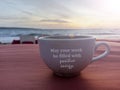 Inspirational quote and text wishes - may your week be filled with positive energy. Text on white cup on red table in the beach.