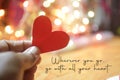 Inspirational quote - Wherever you go, go with all your heart. On pink and white bokeh light background with hand holding red love