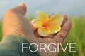 Inspirational single word - forgive. With woman holding a yellow Bali frangipani flower in hand on background of blue sky.