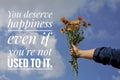 Inspirational word - You deserve happiness even if you are not used to it. Hand with flowers againts bright and clean blue sky Royalty Free Stock Photo