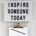 `Inspire someone today` words, clipboard with blank sheet of paper on a lightbox on a white wooden background, top view. Overhea