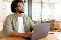 Inspired african-american guy in casual wear and stylish glasses using laptop indoors