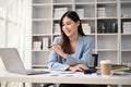 Inspired Asian businesswoman looking at her laptop screen and working at her desk