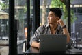 Inspired Asian man daydreaming and looking out the widow while remote working in a coffee shop Royalty Free Stock Photo