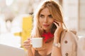 Inspired blonde woman with red scarf drinking coffee in white cup and sharing rumors with friend. Close-up portrait of Royalty Free Stock Photo