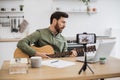 Inspired man playing guitar while recording video on mobile