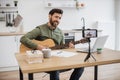 Inspired man playing guitar while recording video on mobile