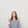 Inspired excited woman with brown hair wearing striped casual shirt standing isolated over gray background raised finger having