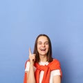 Inspired excited woman wearing white t-shirt and jumper over neck standing isolated over blue background raised finger up has idea