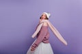 Inspired girl in long scarf funny posing on purple background. Stylish young lady in hat and knitted sweater dancing in Royalty Free Stock Photo