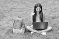 inspired happy child using computer for online school study sitting in park on green grass with backpack, education Royalty Free Stock Photo