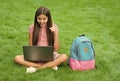 inspired happy child using computer for online school study sitting in park on green grass with backpack, education Royalty Free Stock Photo