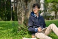 Inspired and happy young Asian male college student sitting under the tree in the park Royalty Free Stock Photo