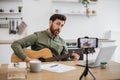 Inspired man playing guitar while recording video on mobile