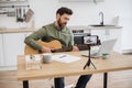 Inspired man playing guitar while recording video on mobile