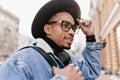 Inspired mulatto man wears casual denim jacket walking down the street. Outdoor photo of african guy in black hat and Royalty Free Stock Photo