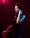 Inspired short haired brunette woman in elegant black dress sits in studio in headphones and sings in microphone Royalty Free Stock Photo